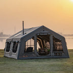 Large camping tent with windows beside a lake at sunset, outdoor gear setup visible inside