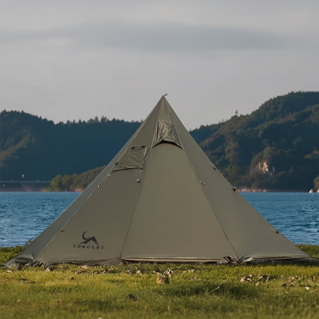 Pyramid camping tent set up by a lake with mountains in the background