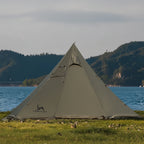 Pyramid camping tent set up by a lake with mountains in the background