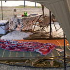 Cozy camping tent interior with picnic table, cooler, chairs and patterned blanket on mat