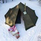 Large green winter camping tent with stove in snowy forest, folding chair and blanket